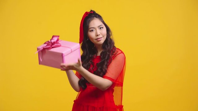 confused and smiling asian girl shaking present isolated on yellow