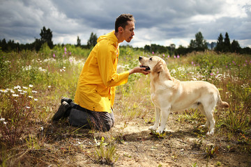 Guy in yellow jacket kissing lovely big dog during walk in filed