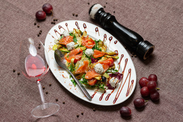 fresh salad with salmon, avocado, cheese and a glass of red wine on a cocoa color textile background