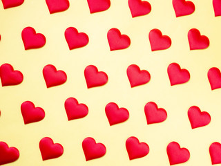 A lot of identical red silk hearts lying staggered on a yellow background. Symbol of love,...