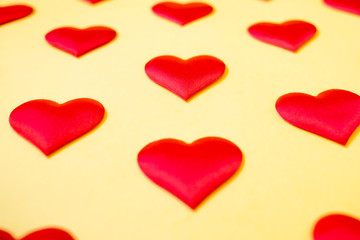 A lot of identical red silk hearts lying staggered on a yellow background. Symbol of love, tenderness and passion