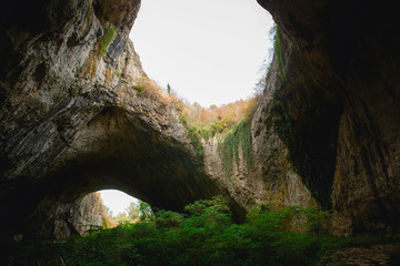 Obraz premium High arches of a huge stone cave with round holes at the top, a tourist road with a fence inside the cave. Bulgaria's natural attraction-Devetashka cave
