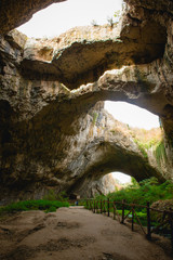 High arches of a huge stone cave with round holes at the top, a tourist road with a fence inside the cave. Bulgaria's natural attraction-Devetashka cave