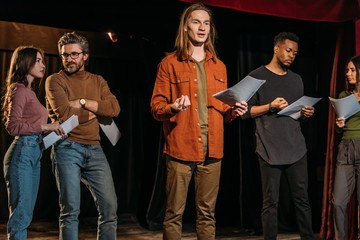 multicultural actors and actresses rehearsing with scripts on stage in theatre