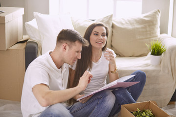 Portrait of happy couple looking at laptop computer together sitting in new house, surrounded with boxes