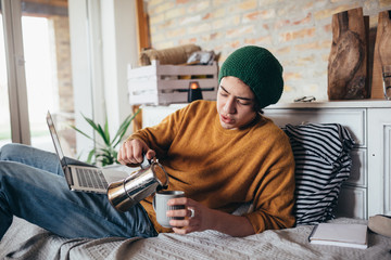 young man drinking coffee and using laptop, relaxing in his room