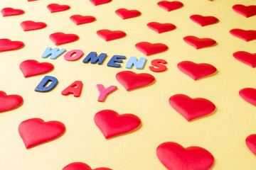 Multi-colored inscription, "Women's Day" in the middle of rhythmically arranged silk red hearts on a yellow background.  Postcard template for International Women's Day