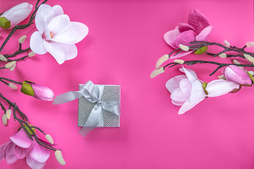 Gift box surprise silver color with a bow on a pink background and artificial orchid flowers.