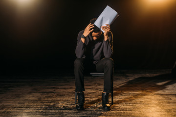stressed african american actor holding scenario on stage during rehearse
