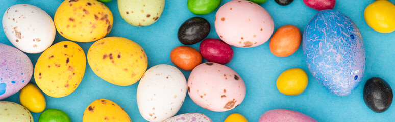 Top view of bright candies, colorful chicken and quail eggs on blue background, panoramic shot