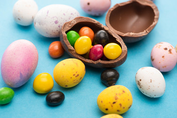 Close up of Easter chicken, quail and chocolate eggs with candies on blue background