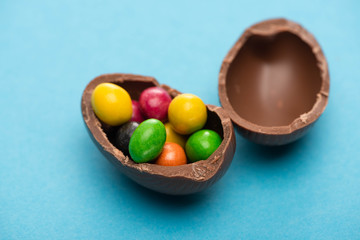Close up view of chocolate Easter egg halves with candies on blue background