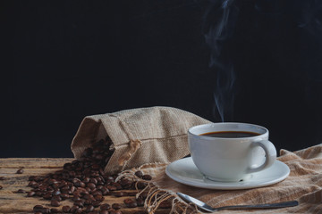 White hot coffee cups and roasted coffee beans on a wooden table have a black backdrop.