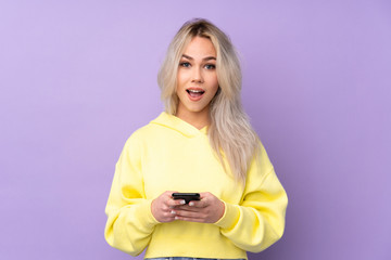 Teenager girl wearing a yellow sweatshirt over isolated purple background surprised and sending a message