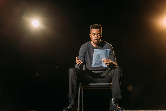 handsome african american actor holding scenario on stage during rehearse