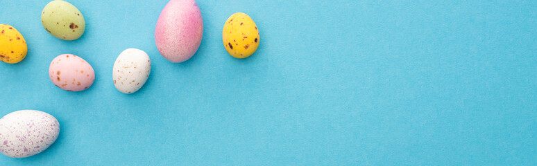 Top view of colorful painted chicken and quail eggs on blue background, panoramic shot