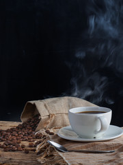 White hot coffee cups and roasted coffee beans on a wooden table have a black backdrop.