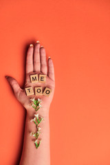 Woman hand on lush lava background covered with flowers and wooden blocks. Me too