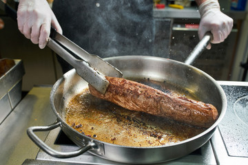 The chef works in the kitchen of the restaurant. Fresh meat roasted in a large frying pan. Restaurant kitchen background