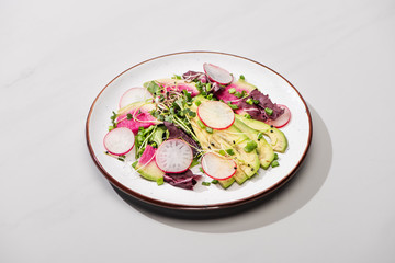 fresh radish salad with greens and avocado on grey surface