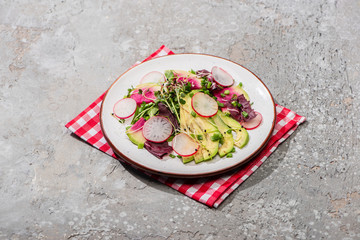 fresh radish salad with greens and avocado on napkin on grey concrete surface
