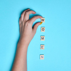 Top view woman hand pointing on women word spelled in wooden blocks on colorful blue background....