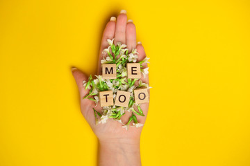 Phrase Me Too made of wooden letters in hand full of flowers on yellow background, top view. Stop sexual assault. Space left for text, copy