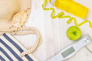 scales, healthy snack, measuring tape and water bottle on a light wooden background. preparation for the summer season and the beach, beach bag, hat and shells, weight loss and sports concept