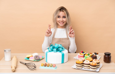 Teenager pastry chef with a big cake in a table with fingers crossing