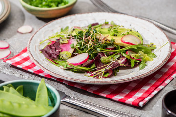fresh radish salad with greens and avocado served on napkin with cutlery near ingredients in bowls on grey concrete surface