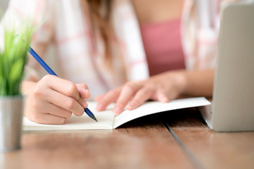 Cropped shot of female hand writing on notebook with pencil.