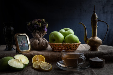 Still life, morning tea with lemons and apples in a homely atmosphere, in dark colors with bright lighting.