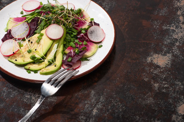 fresh radish salad with greens and avocado on plate on weathered surface with fork