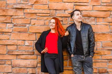 A young man and a girl stand with their backs to a stone wall