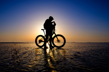 Fototapeta premium Silhouette of bicyclist standing on the clear ice surface of frozen lake in morning backlight