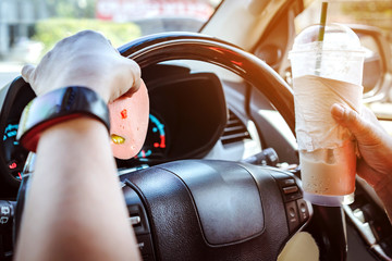 Hungry woman driving her car while eating bologna with ice coffee in the traffic. Selective focus on bologna. © JinnaritT
