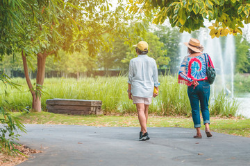 Obraz premium Back view of happiness female friends walking together beside the fountain in the public park.