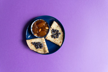Pancake with blueberries, apricot jam with nuts in bowl  on purple background