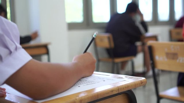 Student hand testing doing test exam with pencil drawing selected choices on answer sheet in school final exams at college or university. Taking multiple choice for assessment in examination classroom