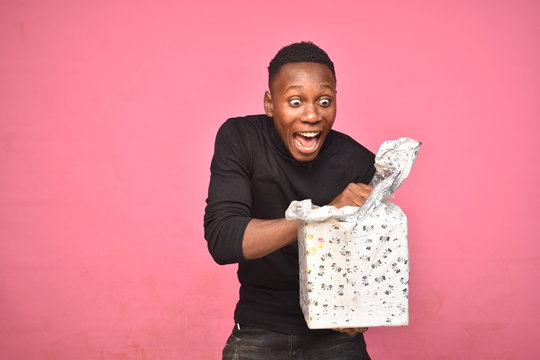 Handsome Young Black Man Opening A Wrapped Present Feeling Happy And Excited