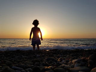 a little boy watching the sunset at the beach.
