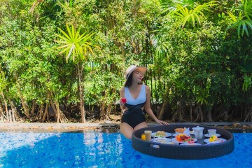 Obraz na płótnie Canvas Portrait beautiful young asian woman happy smile with floating breakfast in tray on swimming pool