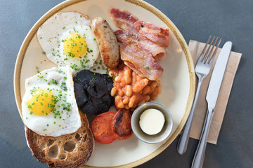 Traditional full English breakfast with fried eggs, sausage, beans, mushroom, grilled tomatoes and bacon on grey tabletop background. Top view