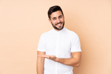Caucasian handsome man isolated on beige background presenting an idea while looking smiling towards