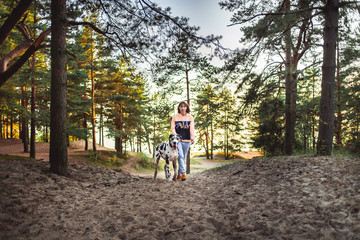 Woman and great Dane dog walking and looking away in forest