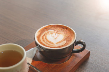 Hot latte art coffee in ceramic cup with tea cup on wooden table background