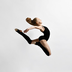 Teenage brunette girl gymnast with pigtail, in black leotard, knee socks and ballet shoes,...