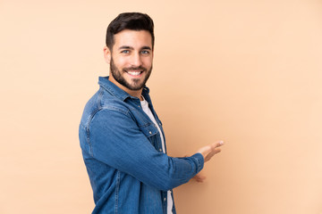 Caucasian handsome man isolated on beige background extending hands to the side for inviting to come