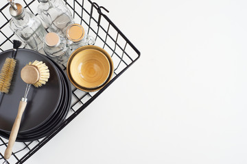 Basket with kitchen utensils, plates, glass bottles, a granny brush for washing dishes, towels on white background. Zero Waste concept. Top view