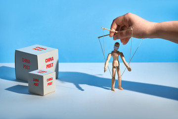 Postal packages, envelopes and parcels from China. Hand holding marionette in face mask. Chinese delivery online stores suffer from fake news and fear to catch COVID-19 from infected package.